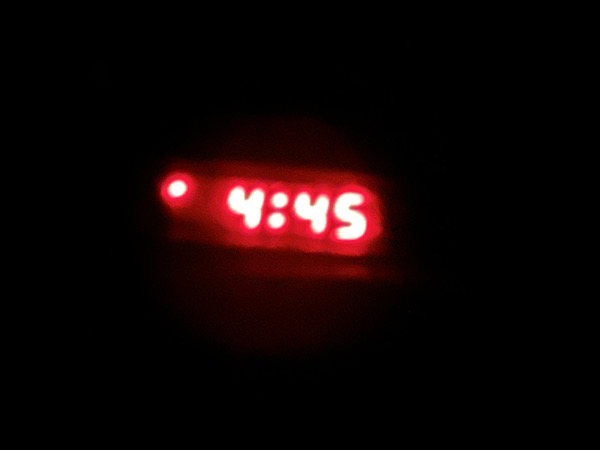 a black photo with the time "4:45" showing in blurry red numbers, as you might see them on a clock radio.